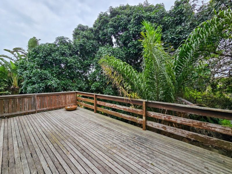 An outdoor timber deck featuring a wooden balustrade, surrounded by mature trees. The deck shows signs of weathering and requires maintenance.