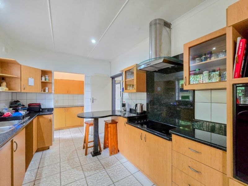 Functional kitchen featuring light wood cabinetry, dark granite countertops, a breakfast bar, and a stainless steel extractor fan with tiled backsplash.