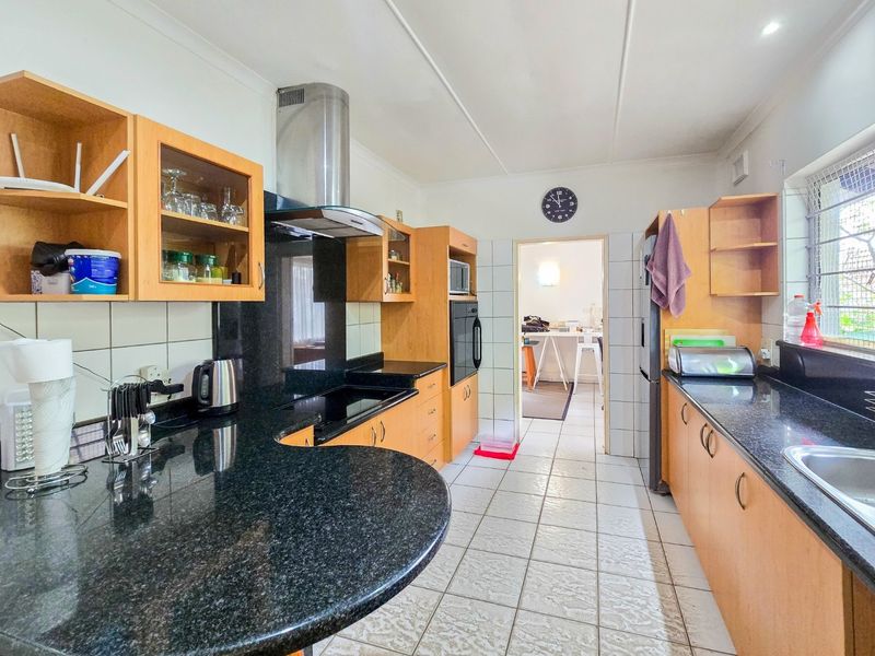 Functional kitchen featuring granite countertops, built-in cabinetry, integrated oven, and extractor fan with tiled flooring and backsplash.
