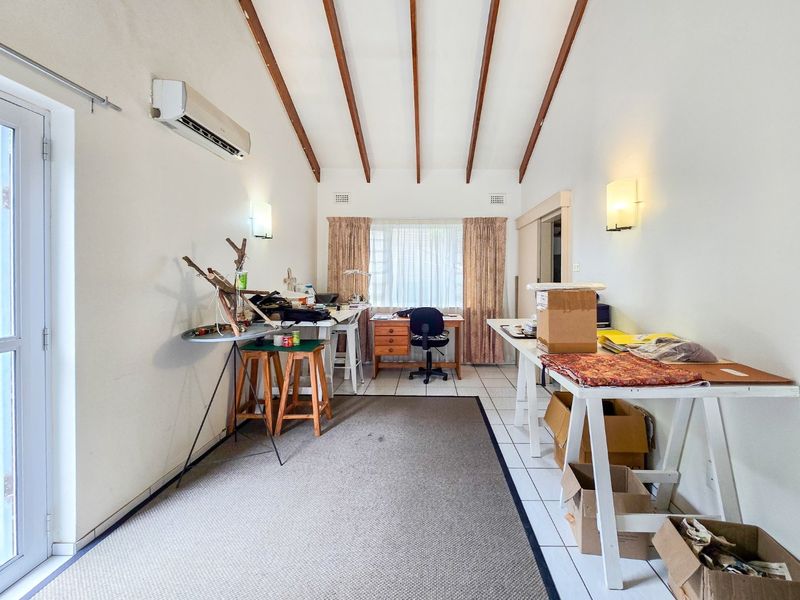 A functional office space featuring exposed timber ceiling beams, tiled flooring, and a split-system air conditioner, offering a versatile area for work or study.
