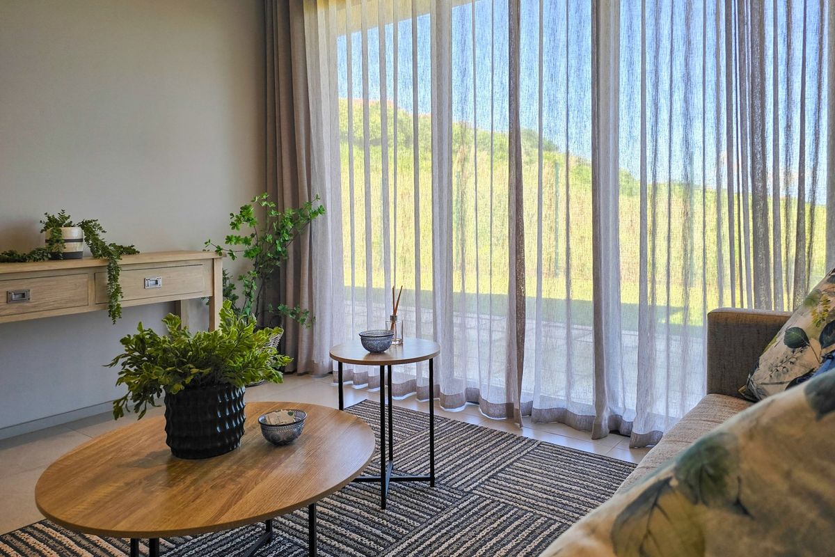 A bright living room featuring large sliding glass doors with sheer curtains, providing ample natural light and a view of the outdoors.
