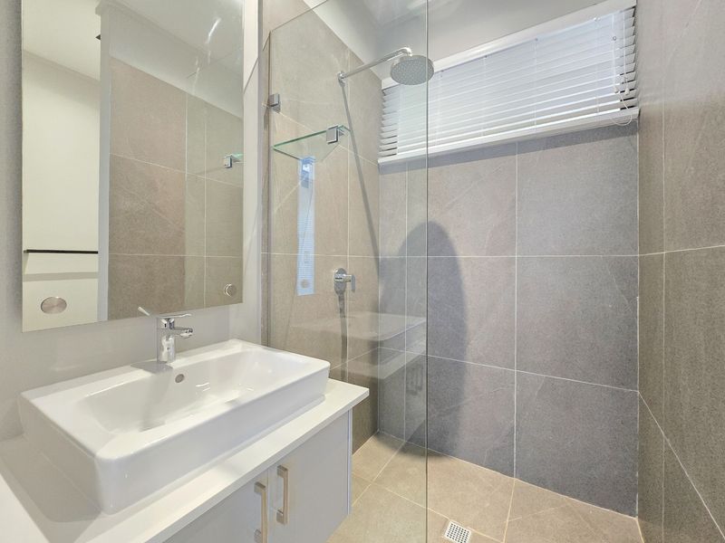 Modern bathroom featuring a sleek vanity with ceramic basin, frameless glass shower enclosure with rain shower head, and neutral large-format porcelain tiling.