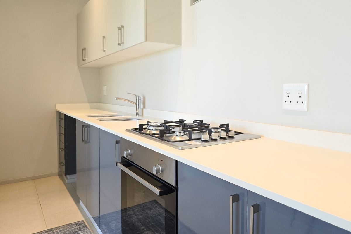 Modern kitchen featuring sleek grey lower cabinetry, white upper cabinets, stone countertops, a gas hob, and a built-in oven.