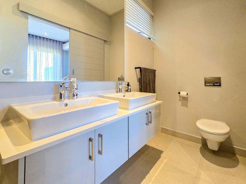 Modern bathroom featuring a double vanity with vessel sinks, large wall mirror, wall-mounted toilet with concealed cistern, and neutral tiled flooring.