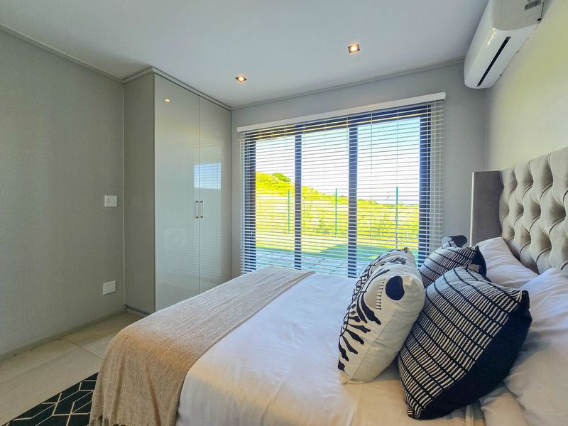 Modern bedroom featuring built-in cupboards, recessed downlighting, air conditioning, and large windows with venetian blinds overlooking the exterior.
