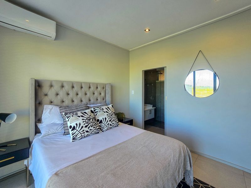 A well-maintained bedroom featuring tiled flooring, recessed lighting, a wall-mounted air conditioning unit, and direct access to an en-suite bathroom.
