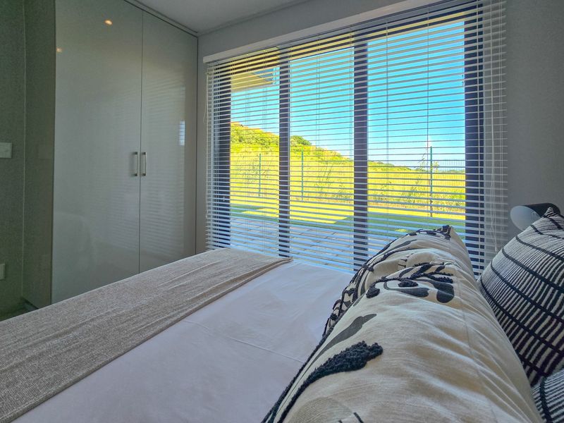 A modern bedroom featuring a built-in wardrobe, venetian blinds, and a large sliding glass door providing natural light and views of the outdoor landscape.