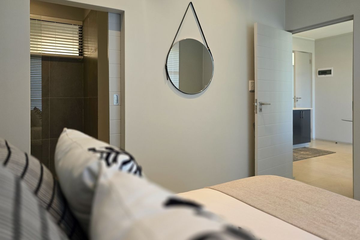 A well-maintained bedroom featuring neutral tones, tiled flooring, and direct access to an en-suite bathroom and adjacent living area.