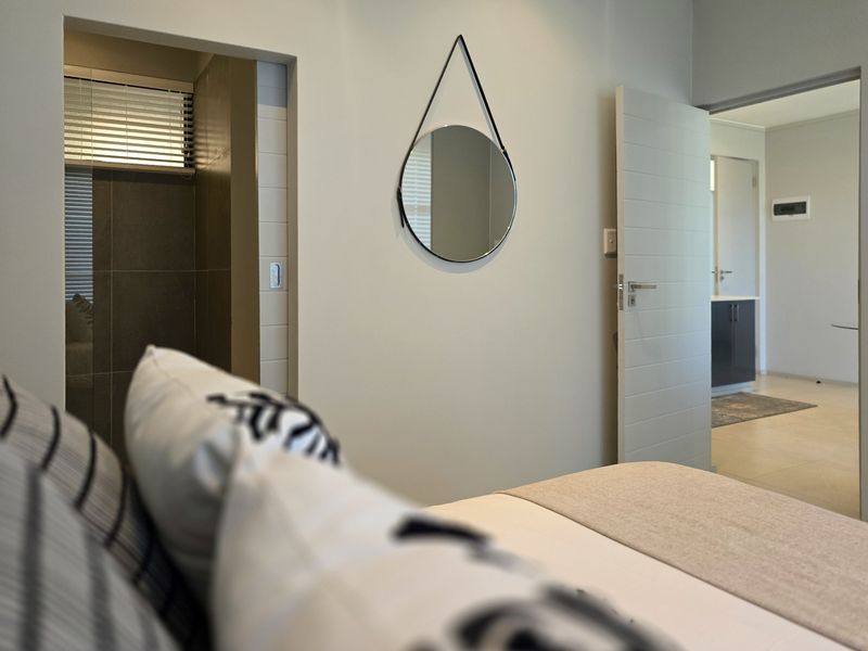 A well-maintained bedroom featuring neutral tones, tiled flooring, and direct access to an en-suite bathroom and adjacent living area.