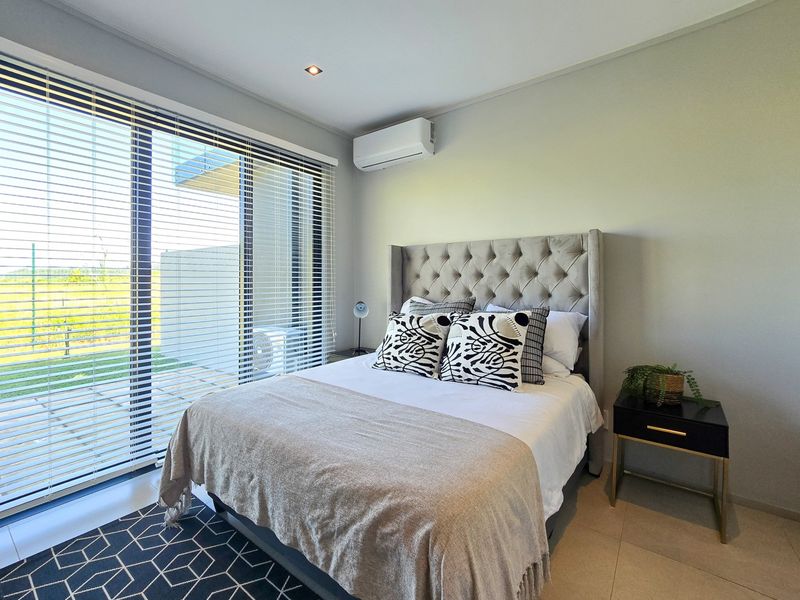 A modern, well-maintained bedroom featuring tiled flooring, recessed lighting, a split-system air conditioner, and large sliding glass doors providing natural light.