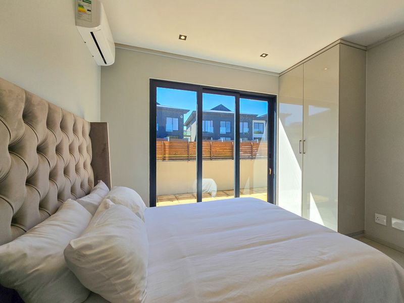 Modern bedroom featuring built-in high-gloss cupboards, recessed lighting, split-system air conditioning, and large sliding glass doors leading to an outdoor area.