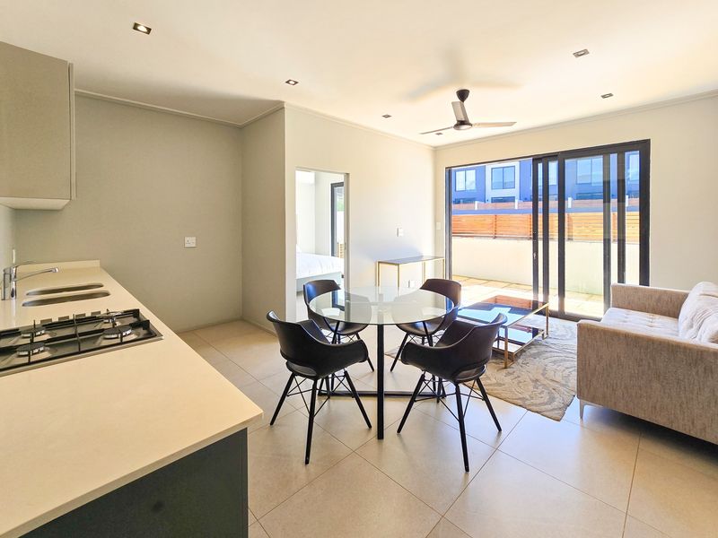 Modern open-plan living area featuring a sleek kitchen with stone countertops, gas hob, and seamless flow to a private balcony through sliding glass doors.