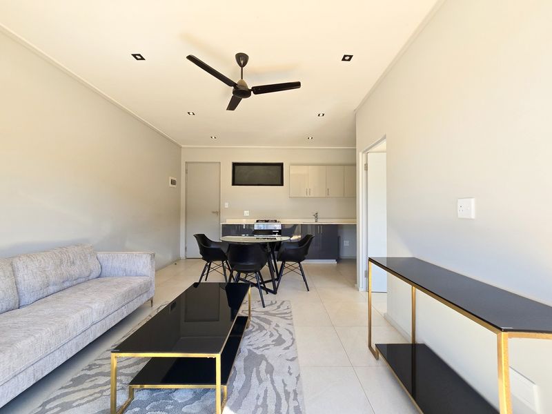 Modern open-plan living area featuring tiled floors, recessed lighting, a ceiling fan, and a compact kitchen with built-in cabinetry and stove.