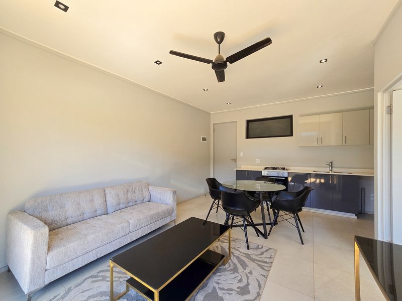 Modern open-plan living area featuring a compact kitchen with built-in cabinetry, gas hob, oven, and tiled flooring throughout.