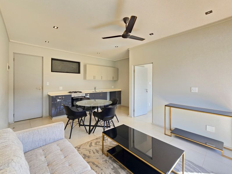 Modern open-plan living area featuring a sleek kitchen with built-in cabinetry, gas hob, and oven, complemented by neutral tiled flooring and recessed lighting.