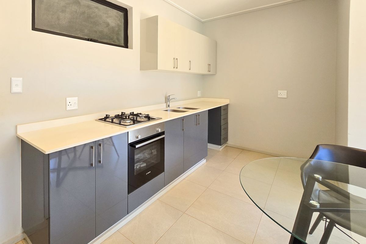 Modern kitchen featuring sleek grey and white cabinetry, stone countertops, a built-in gas hob, and an integrated oven.