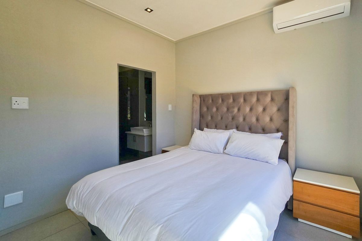 A well-maintained bedroom featuring tiled flooring, recessed lighting, an integrated air conditioning unit, and direct access to an en-suite bathroom.