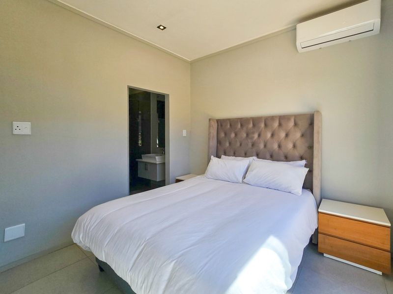 A well-maintained bedroom featuring tiled flooring, recessed lighting, an integrated air conditioning unit, and direct access to an en-suite bathroom.