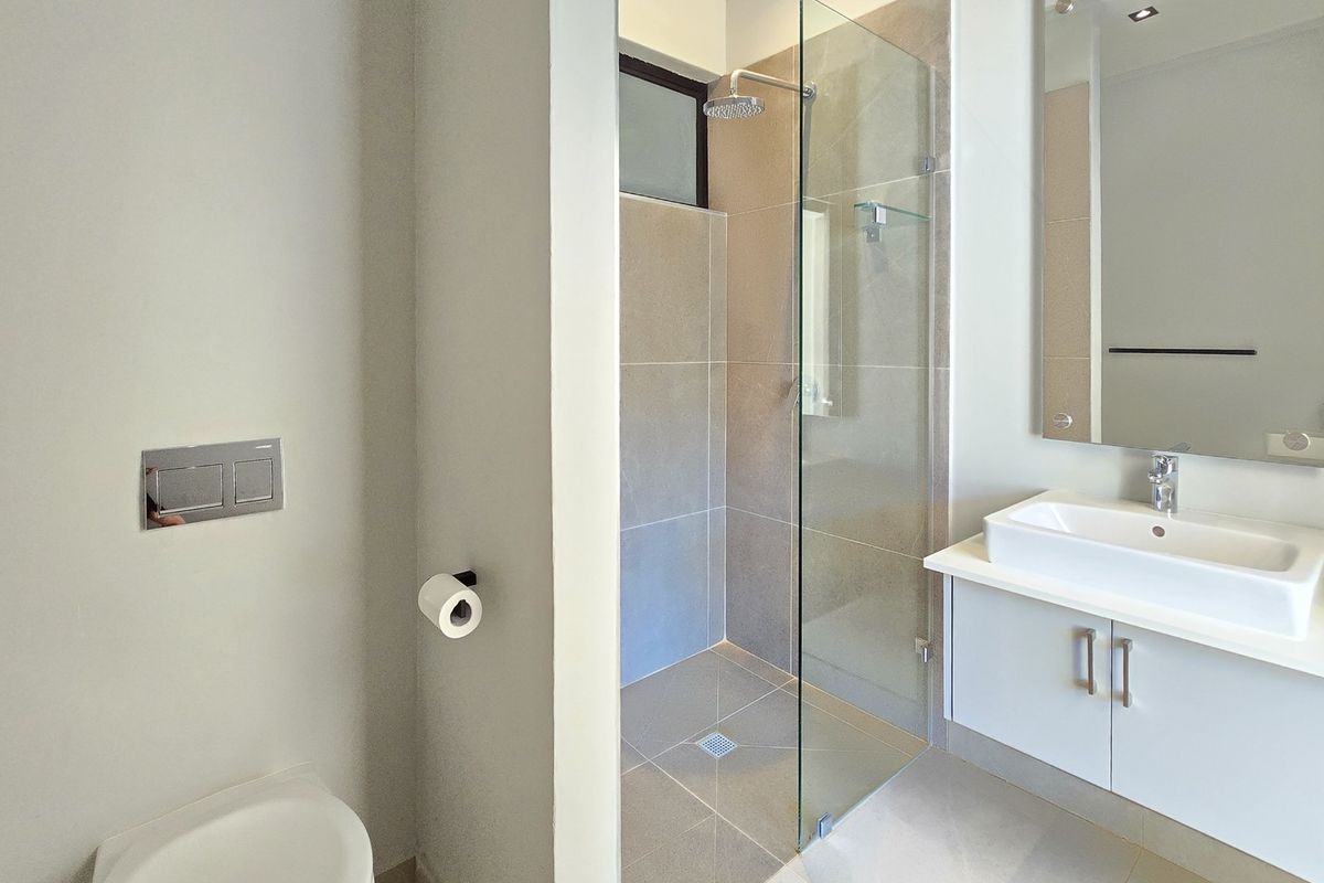 Modern bathroom featuring a wall-mounted toilet, a glass-enclosed shower with a rain shower head, and a sleek vanity with a vessel sink.