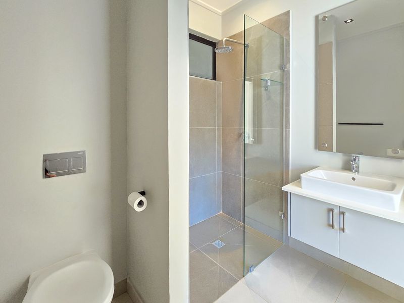 Modern bathroom featuring a wall-mounted toilet, a glass-enclosed shower with a rain shower head, and a sleek vanity with a vessel sink.
