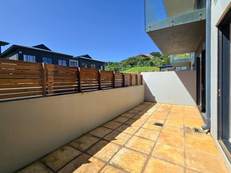A private outdoor patio area featuring tiled flooring, a timber privacy screen, and a glass balustrade, offering a clean space for outdoor relaxation.