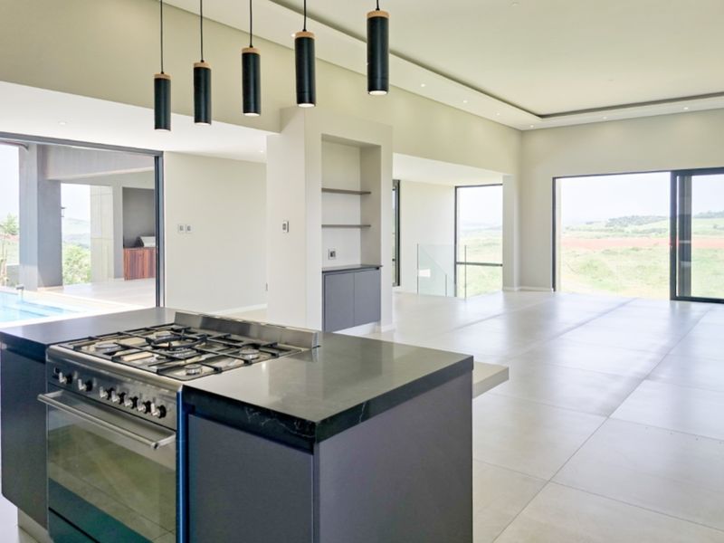 Spacious open-plan living and kitchen area featuring a modern gas stove, sleek stone countertops, large sliding doors, and neutral tiled flooring throughout.