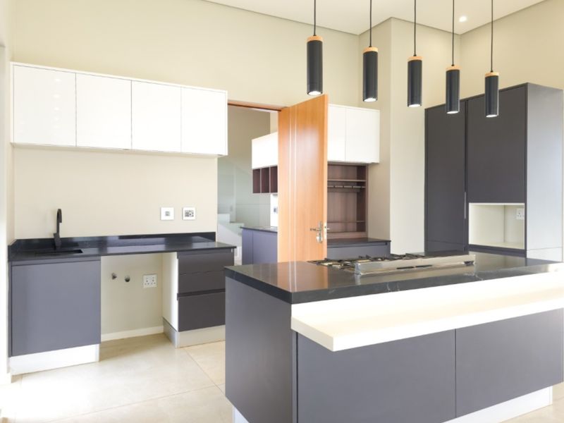 Modern kitchen featuring a central island with a gas hob, sleek dark cabinetry, stone countertops, and contemporary pendant lighting in an open-plan layout.