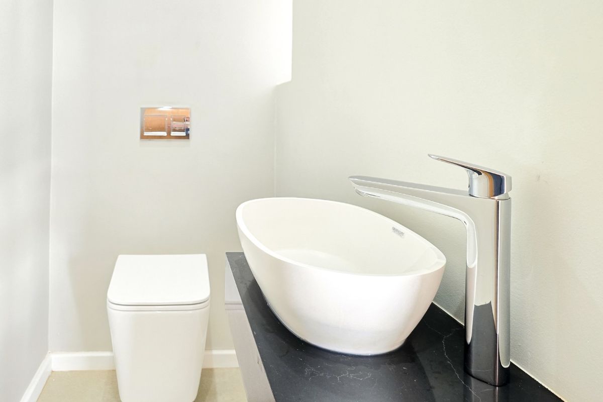 Modern bathroom featuring a wall-hung toilet, sleek vessel sink with chrome mixer tap, and a dark stone vanity countertop.