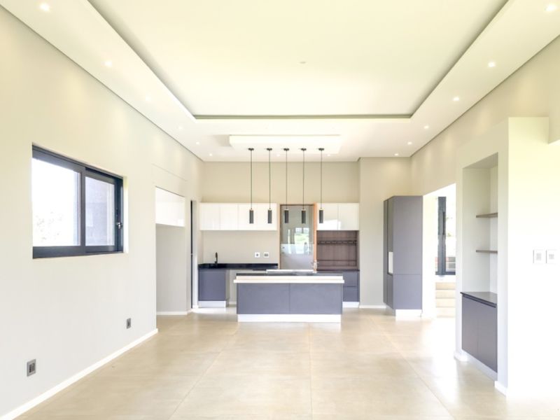 Spacious open-plan kitchen area featuring modern cabinetry, a central island, recessed ceiling lighting, and neutral tiled flooring in a contemporary, minimalist setting.
