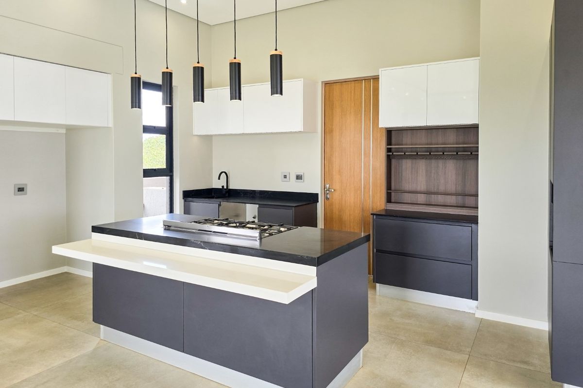 Modern kitchen featuring a central island with a gas hob, sleek two-tone cabinetry, stone countertops, and contemporary pendant lighting.