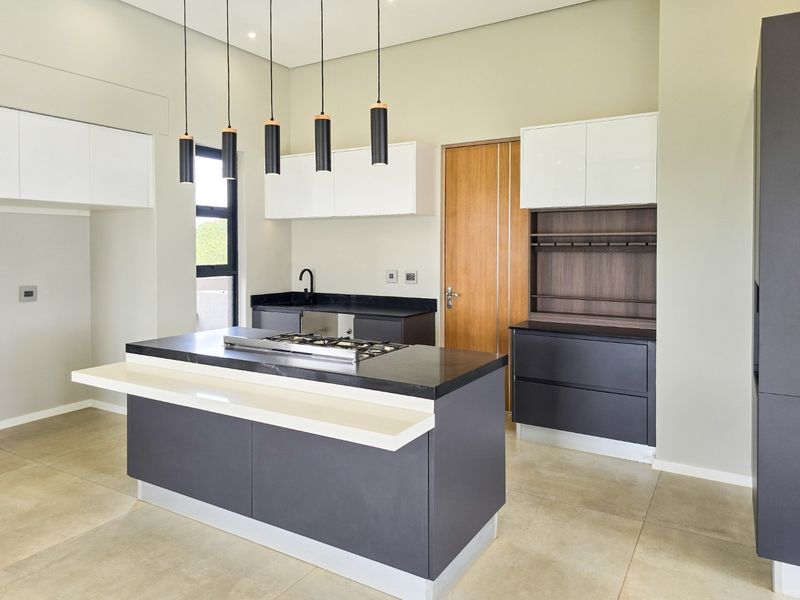 Modern kitchen featuring a central island with a gas hob, sleek two-tone cabinetry, stone countertops, and contemporary pendant lighting.