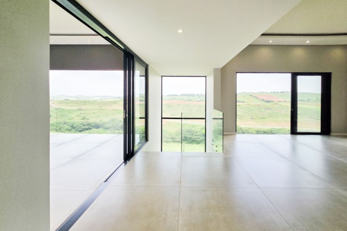 Spacious, modern open-plan living area featuring large format floor tiles, recessed lighting, and expansive sliding glass doors opening to scenic landscape views.