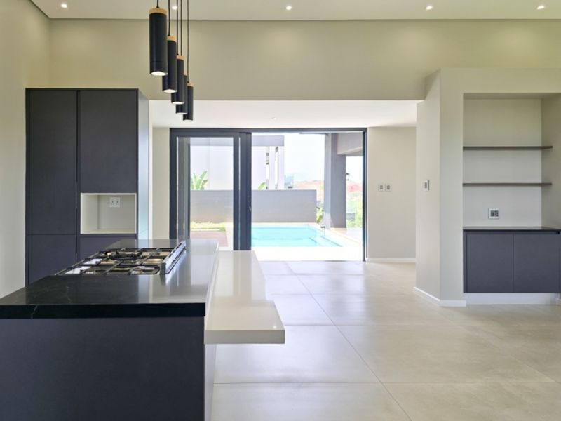 Modern open-plan kitchen featuring a central island with gas hob, sleek cabinetry, and seamless flow to the outdoor pool area through sliding glass doors.