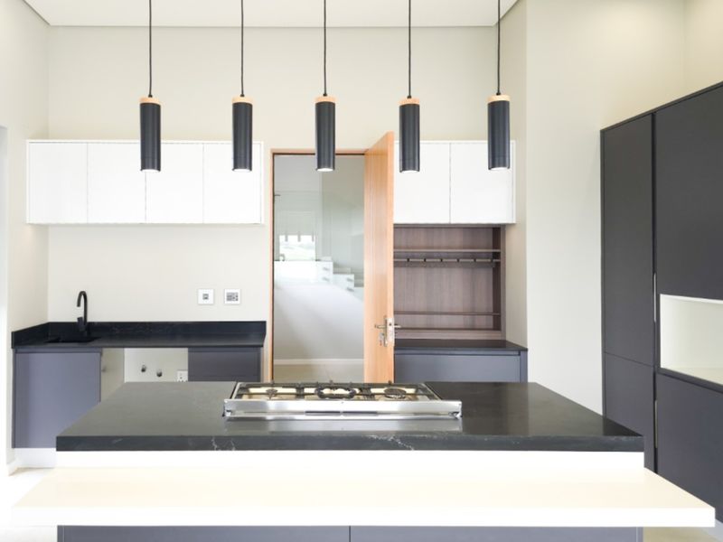 Modern kitchen featuring a central island with a gas cooktop, sleek two-tone cabinetry, stone countertops, and contemporary pendant lighting.