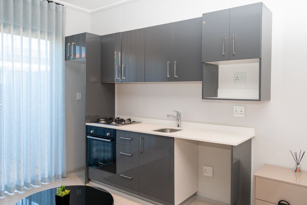 Modern kitchen featuring high-gloss grey cabinetry, stone countertops, a built-in gas hob, oven, and integrated sink with dedicated appliance space.