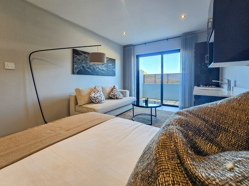Modern open-plan studio apartment featuring a kitchenette, living area, and sliding glass doors leading to a private balcony.