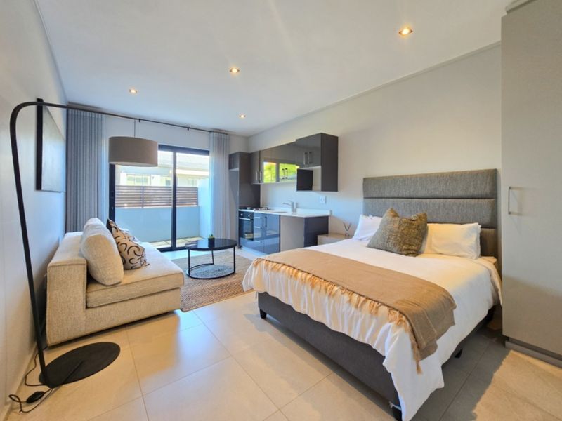 Modern open-plan studio apartment featuring a compact kitchenette with built-in appliances, tiled flooring, and direct access to a private balcony.