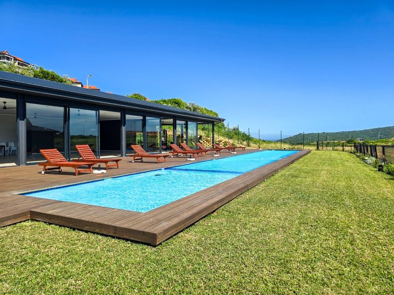 A modern outdoor swimming pool area featuring extensive timber decking, large sliding glass doors leading to the interior, and well-maintained lawn surroundings.