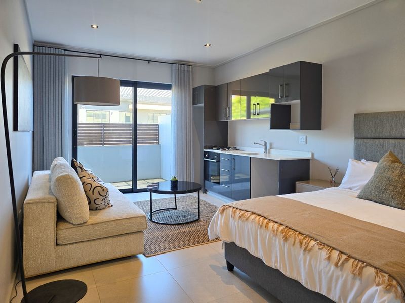 Modern open-plan studio apartment featuring a compact kitchenette with built-in cabinetry, integrated appliances, and direct access to a private balcony.