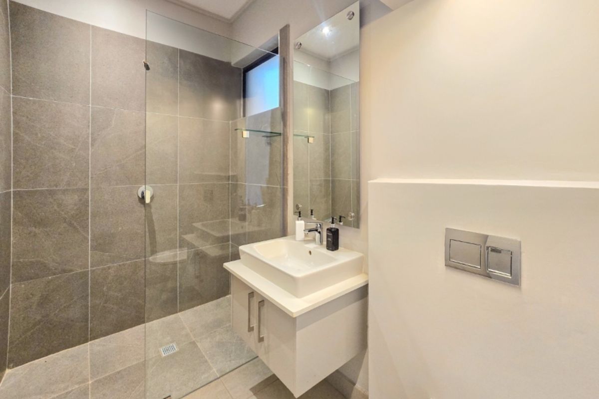 Modern bathroom featuring a walk-in shower with glass screen, wall-mounted vanity with basin, and a concealed cistern flush plate.