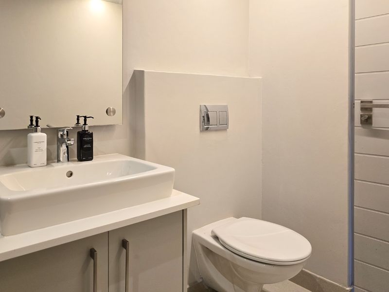 A modern bathroom featuring a wall-mounted toilet with a concealed cistern, a vanity cabinet with a basin, and a wall-mounted mirror.