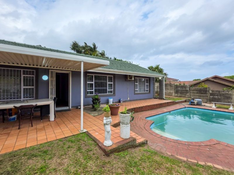 Rear exterior view featuring a swimming pool, covered patio area with tiled flooring, and a concrete boundary wall.