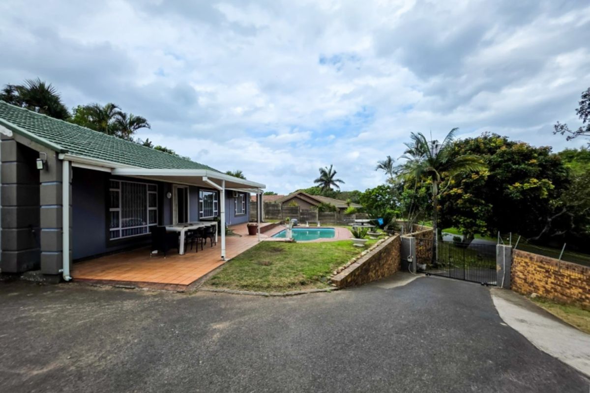 Rear exterior view featuring a swimming pool, covered patio area, and paved driveway with surrounding garden and boundary walls.
