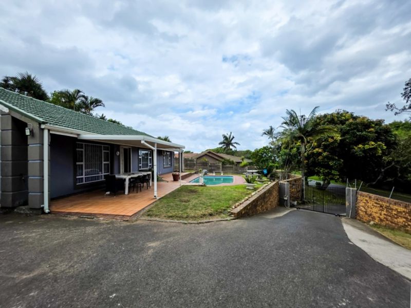 Rear exterior view featuring a swimming pool, covered patio area, and paved driveway with surrounding garden and boundary walls.