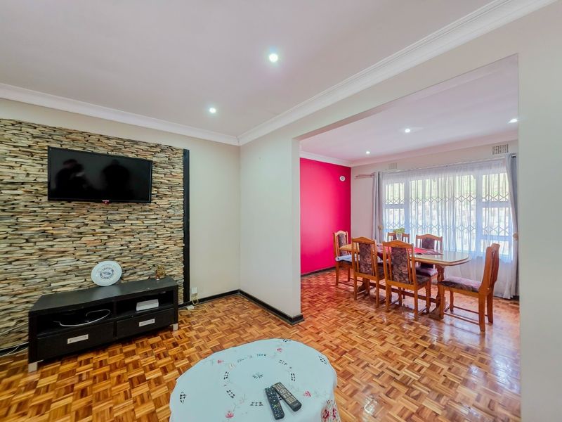 Open-plan living and dining area featuring parquet flooring, a stone feature wall, and recessed downlighting.