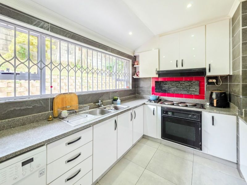 A functional kitchen featuring white cabinetry, granite countertops, a double basin sink, built-in oven, and electric hob with a red tiled splashback.