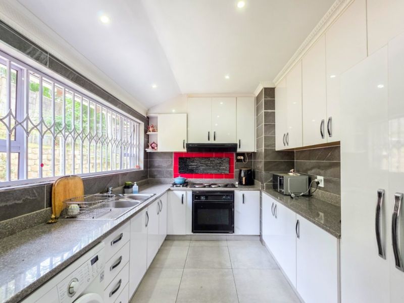Modern kitchen featuring white cabinetry, granite countertops, built-in oven with gas hob, and tiled flooring with ample natural light.