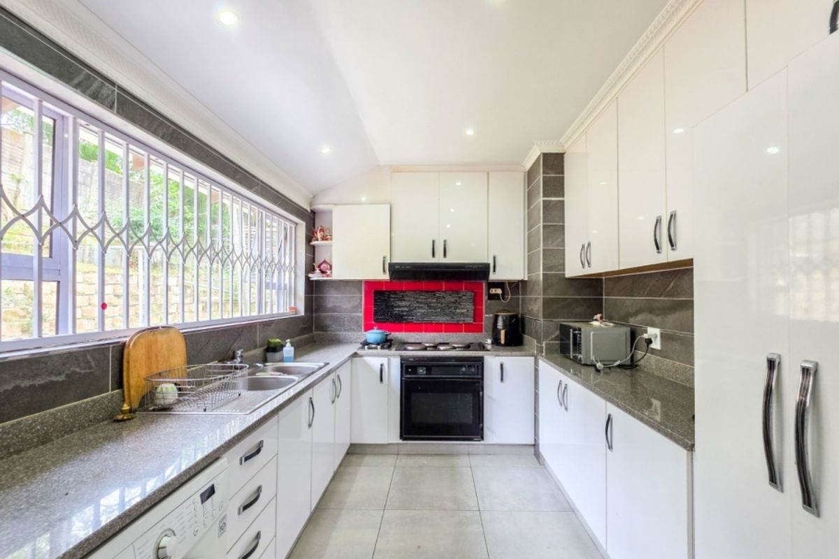 Modern kitchen featuring white cabinetry, granite countertops, built-in oven with gas hob, and tiled flooring with ample natural light.
