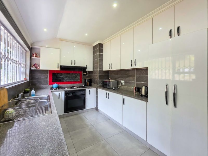 A functional kitchen featuring white high-gloss cabinetry, stone countertops, a double sink, and built-in cooking appliances with a tiled backsplash.