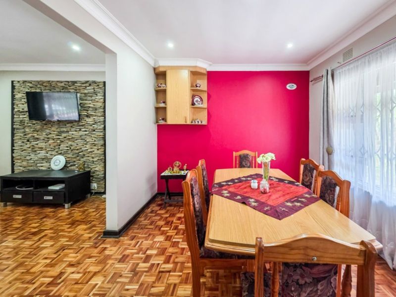 Open-plan dining and living area featuring warm parquet flooring, a striking stone feature wall, and built-in cabinetry, creating a functional and connected living space.